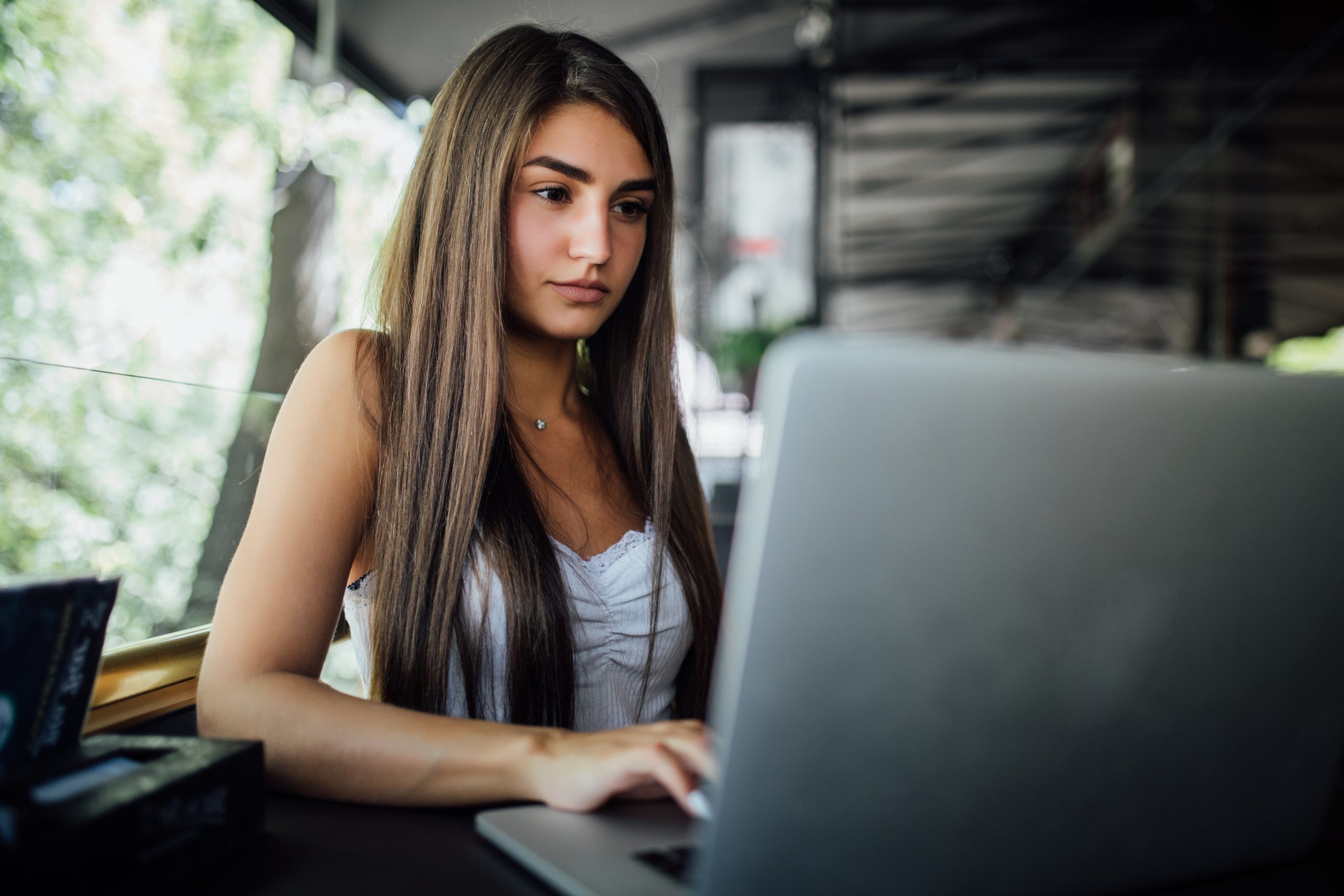 Pretty smiling model girl works on her laptop in the cafe daytilme terrace